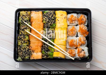 Set di panini di sushi con salmone e verdure in vassoio nero e bacchette di legno sulle tavole. Piatti asiatici di pesce. Cucina tradizionale giapponese, cu Foto Stock