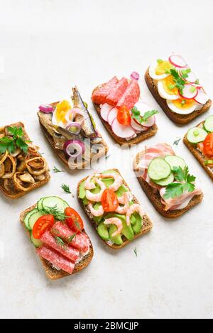 Set di diversi panini con carne, verdure e pesce. Assortimento di panini aperti su fondo in pietra chiara. Gustoso snack salutare. Foto Stock