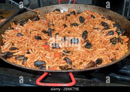 Pesce fresco, pasta di pomodoro, penne cucinate in un grande piatto di wok durante il brunch a buffet all'aperto nel giardino vicino alla piscina. Buffet di cibo fresco Foto Stock