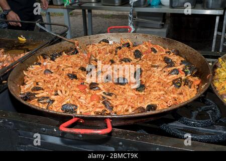 Pesce fresco, pasta di pomodoro, penne cucinate in un grande piatto di wok durante il brunch a buffet all'aperto nel giardino vicino alla piscina. Buffet di cibo fresco Foto Stock