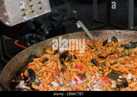 Pesce fresco, pasta di pomodoro, penne cucinate in un grande piatto di wok durante il brunch a buffet all'aperto nel giardino vicino alla piscina. Buffet di cibo fresco Foto Stock