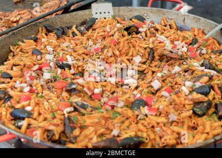 Pesce fresco, pasta di pomodoro, penne cucinate in un grande piatto di wok durante il brunch a buffet all'aperto nel giardino vicino alla piscina. Buffet di cibo fresco Foto Stock