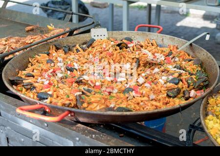 Pesce fresco, pasta di pomodoro, penne cucinate in un grande piatto di wok durante il brunch a buffet all'aperto nel giardino vicino alla piscina. Buffet di cibo fresco Foto Stock