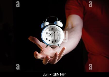 Orologio con sveglia bianco retro che si sovrappone sopra la mano maschile caucasica su sfondo scuro con spazio per le copie Foto Stock