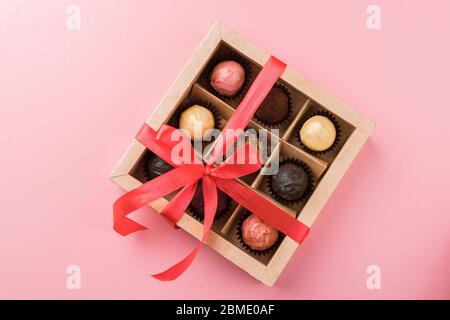 Set di diversi cioccolatini in una scatola di carta con un nastro viola satinato su uno sfondo luminoso. Concetto di vacanza. Foto Stock