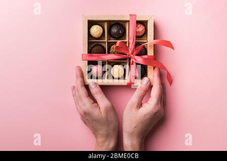 Una donna si stanca un arco e apre una scatola di cioccolatini. Set di diversi cioccolatini in una scatola di carta a mani femminili. Foto Stock