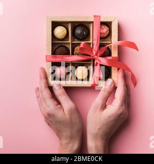 Una donna si stanca un arco e apre una scatola di cioccolatini. Set di diversi cioccolatini in una scatola di carta a mani femminili. Foto Stock