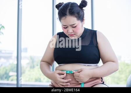 Donna in sovrappeso asiatico che misura lo strato grasso con la linea della vita a casa Foto Stock