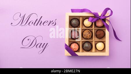 Set di diversi cioccolatini in una scatola di carta con un nastro di raso su uno sfondo luminoso iscrizione Festa della mamma. Foto Stock