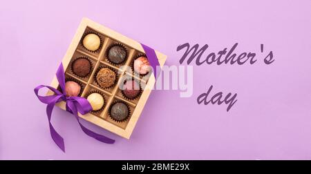 Set di diversi cioccolatini in una scatola di carta con un nastro di raso su uno sfondo luminoso iscrizione Festa della mamma. Foto Stock