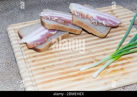 Pancetta affumicata, pane, cipolla verde su un tagliere di legno Foto Stock