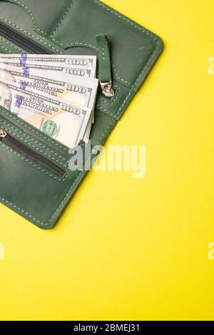 Diverse centinaia di banconote da dollaro sporgono da un elegante portafoglio in pelle verde su uno sfondo giallo brillante. Vista dall'alto con spazio libero Foto Stock