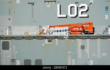 Un ascensore di accesso elevato picker rosso ciliegia su una nave da guerra nel porto Foto Stock