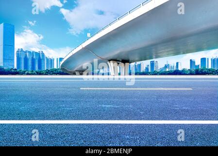 Sotto il cavalcavia, strada asfaltata senza auto, moderno skyline della città come sfondo. Foto Stock