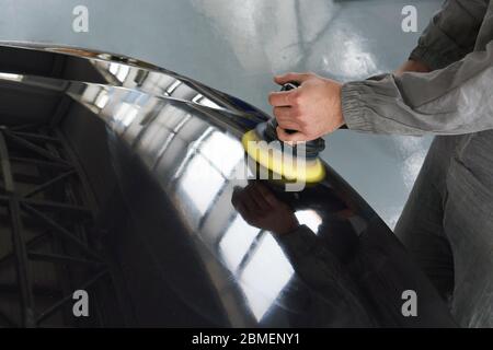 Primo piano del lavoratore mani con lucidatrice per lucidare una carrozzeria grigia in officina, Auto Mechanic Polishing Car Foto Stock