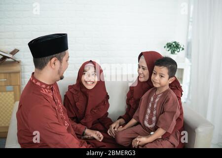 Famiglia asiatica che indossa abiti tradizionali malesi seduti sul divano con il concetto di Eid Mubarak Foto Stock