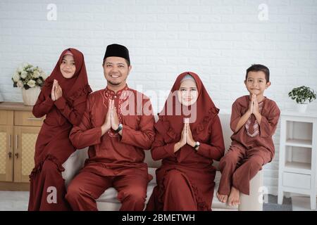 La famiglia musulmana asiatica che indossa abiti malesi tradizionali desidera l'Eid Mubarak felice quando si siede insieme sul divano Foto Stock