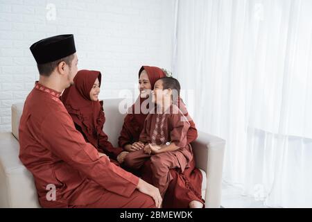 Famiglia asiatica che indossa abiti tradizionali malesi seduti sul divano con il concetto di Eid Mubarak Foto Stock