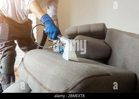 Servizio di pulizia. Uomo janitor in guanti e uniforme aspirapolvere divano con attrezzature professionali Foto Stock