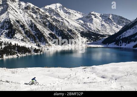 Ciclista giostre a neve a riva del lago di montagna ad Almaty in Kazakistan Foto Stock