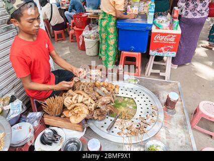 Yangon Myanmar - Ottobre 26 2013; giovane uomo in maglietta rossa prepara cibo di strada per vendere in città strada, Foto Stock