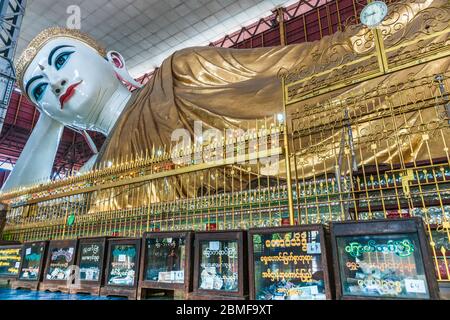 Yangon Myanmar - Ottobre 26 2013; grande Buddha reclinato in abiti d'oro che giace sopra una fila di scatole di donazione con denaro. Foto Stock