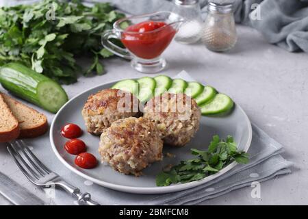 Tagli di manzo serviti con cetrioli e salsa di pomodoro su un piatto grigio su fondo grigio in cemento, formato orizzontale Foto Stock