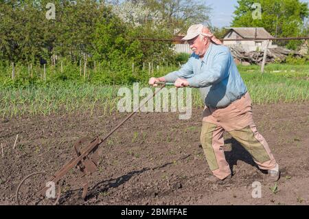 Anziani ucraini senior contadino che lavora con aratro a mano in giardino cucina nella stagione primaverile Foto Stock