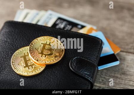 Portafoglio nero con banconote, carte elettroniche e bitcoins su sfondo ligneo. Simbolo di prosperità e prosperità. Primo piano Foto Stock