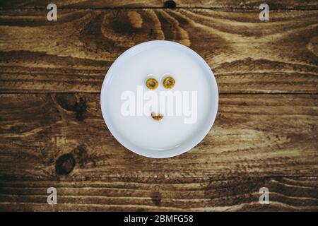 Una ciotola con appena due e mezzo pezzi di cereali rotondi a sinistra che creano l'aspetto di un viso nel latte Foto Stock