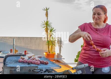 Donna rossa in camicia rossa con glitter che fa barbecue sulla terrazza della sua casa Foto Stock
