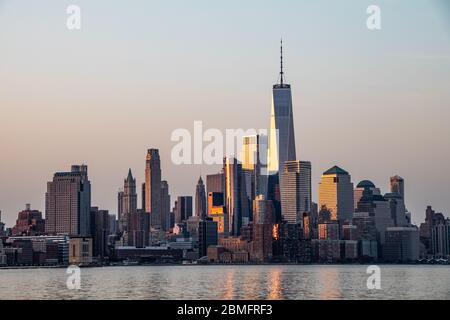 Gli edifici nel quartiere finanziario di Manhattan iniziano a riflettere il sole che sorge attraverso l'Hudson Foto Stock