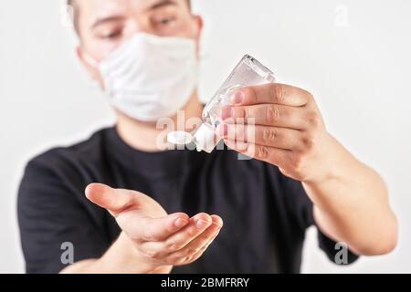 Giovane uomo mani tenendo il gel antibatterico di sfregamento circa per cadere e pulire, faccia sfocata con la maschera del naso della bocca sullo sfondo. Può essere usato come coronavirus Foto Stock