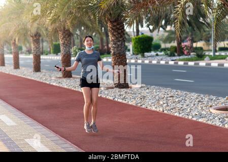 Donna asiatica che si esercita con una corda di salto e indossa la maschera chirurgica protettiva all'aperto Foto Stock