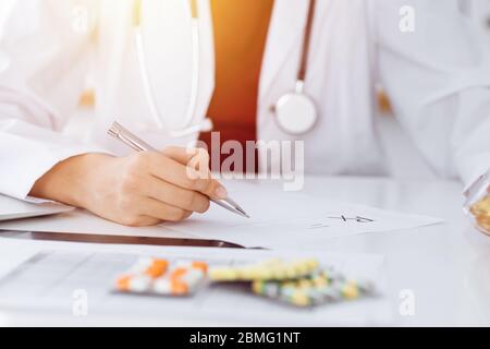 Donna-medico sconosciuto riempie in su la forma di prescrizione in stanza soleggiata, primo piano Foto Stock