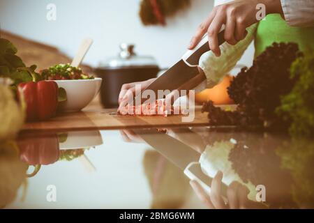 Unknown mani umane per la cottura in cucina. La donna per affettare il pomodoro rosso. Pasto sano e cibo vegetariano concept Foto Stock