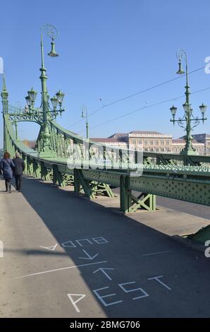 Coppia passando il ponte liberty con adesivo di buda e peste su di esso. Szabadság híd a Budapest, Ungheria, collega Buda e Pest attraverso il Danubio. Foto Stock