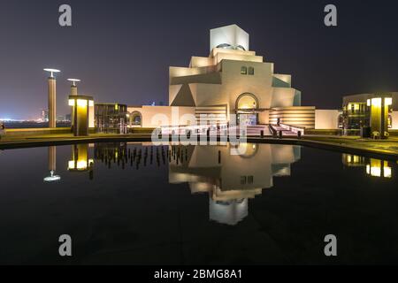 Visita del Museo d'Arte Islamica del Qatar a Doha che si specchiano in acqua di stagno di notte. Architettura futuristica vicino alla baia di Doha. Foto Stock