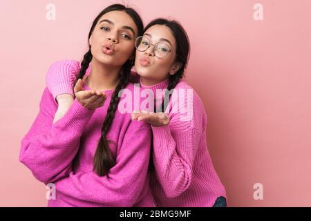 Immagine di due ragazze adolescenti felici con trecce in abiti casual sorridente e soffiare aria bacio a voi isolato su sfondo rosa Foto Stock