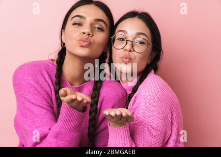 Immagine di due ragazze adolescenti felici con trecce in abiti casual sorridente e soffiare aria bacio a voi isolato su sfondo rosa Foto Stock