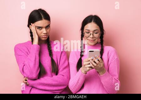 Immagine di ragazza offesa sconvolto teenage in piedi da suo amico felice femmina con cellulare isolato su sfondo rosa Foto Stock