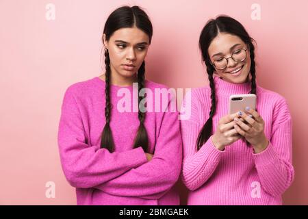 Immagine di ragazza offesa sconvolto teenage in piedi da suo amico felice femmina con cellulare isolato su sfondo rosa Foto Stock