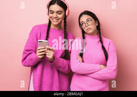 Immagine di ragazza offesa sconvolto teenage in piedi da suo amico felice femmina con cellulare isolato su sfondo rosa Foto Stock