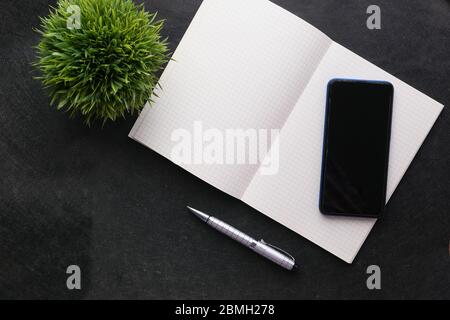 Vista dall'alto dello smartphone con schermo vuoto e blocco note su sfondo nero Foto Stock