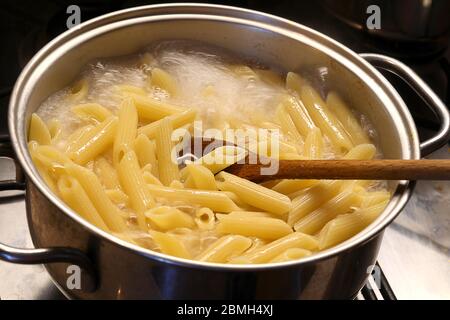 Pentola con acqua bollente e la pasta italiana durante la cottura e un  cucchiaio di legno da mescolare Foto stock - Alamy