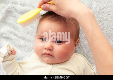 La mamma pettina un neonato con una speciale spazzola per capelli. Igiene del bambino Foto Stock