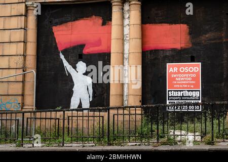 MERTHYR TYDFIL, GALLES - 09 MAGGIO 2020: Silhouette dipinta di un uomo che sventola una bandiera rossa su un vecchio edificio vuoto a Merthyr Tydfil. Foto Stock