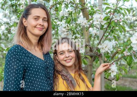 Famiglia felice, mamma e figlia in abiti eleganti vicino all'albero fiorente guardando la macchina fotografica Foto Stock