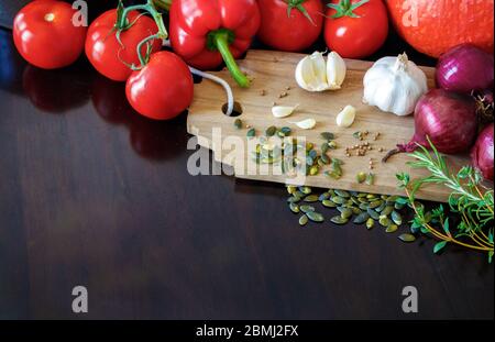 Composizione di verdure, erbe, spezie, semi e uova su un tagliere di legno. Sono visibili: Pomodori di vite, pepe, zucca, aglio, cipolle rosse, cotta Foto Stock