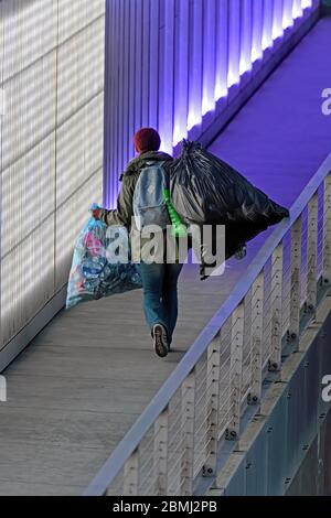 Una donna da sola che trasporta grandi sacchetti di riciclabili attraverso un sottopassaggio pedonale di notte Foto Stock